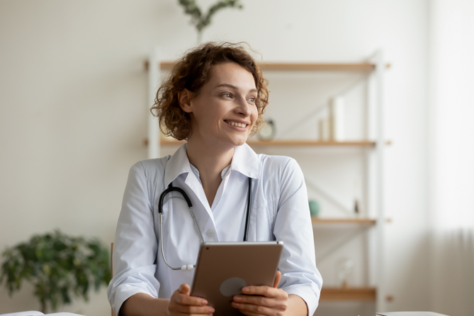 Smiling young female professional doctor holding digital tablet looking away