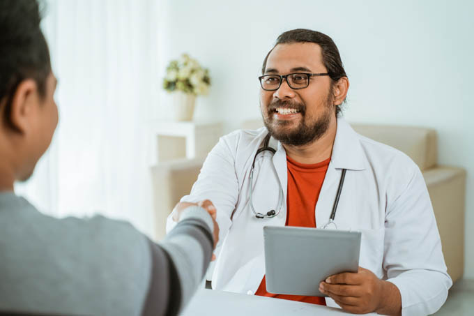 Smiling male doctor shaking hand with male patient in his office