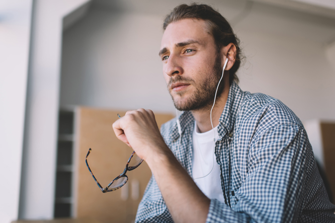 Serious male holding glasses and listening to music in his headphones