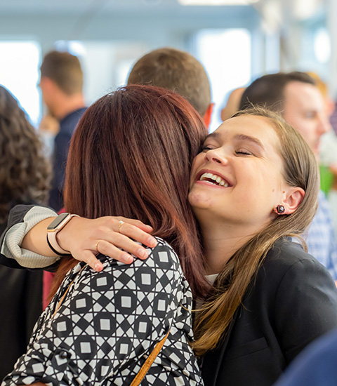 Happy woman hugging a coworker in a busy office