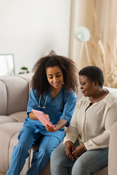 Young female nurse showing a tablet to a female patient sitting on a couch