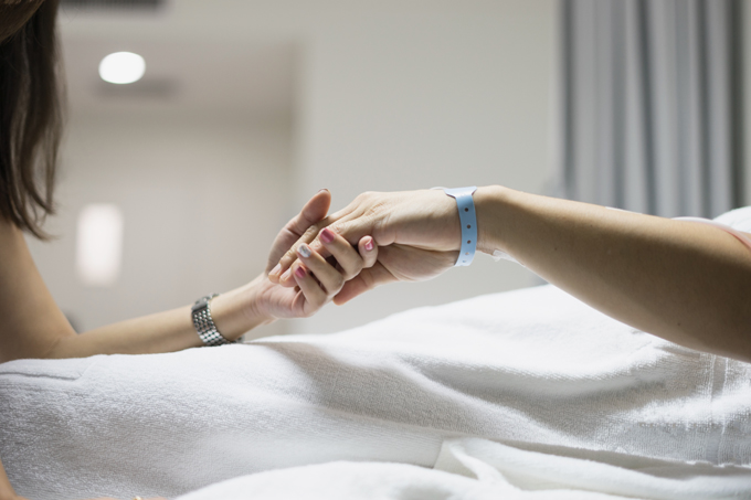 Female holding hand of a female patient in a hospital bed
