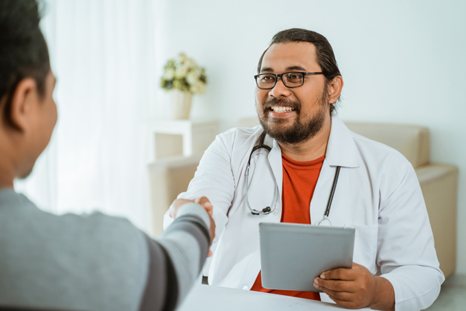 Smiling doctor shaking hand with patient in his office