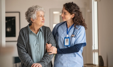 Female nurse helping elderly female patient walk