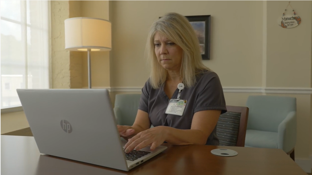 nurse types on laptop in an office