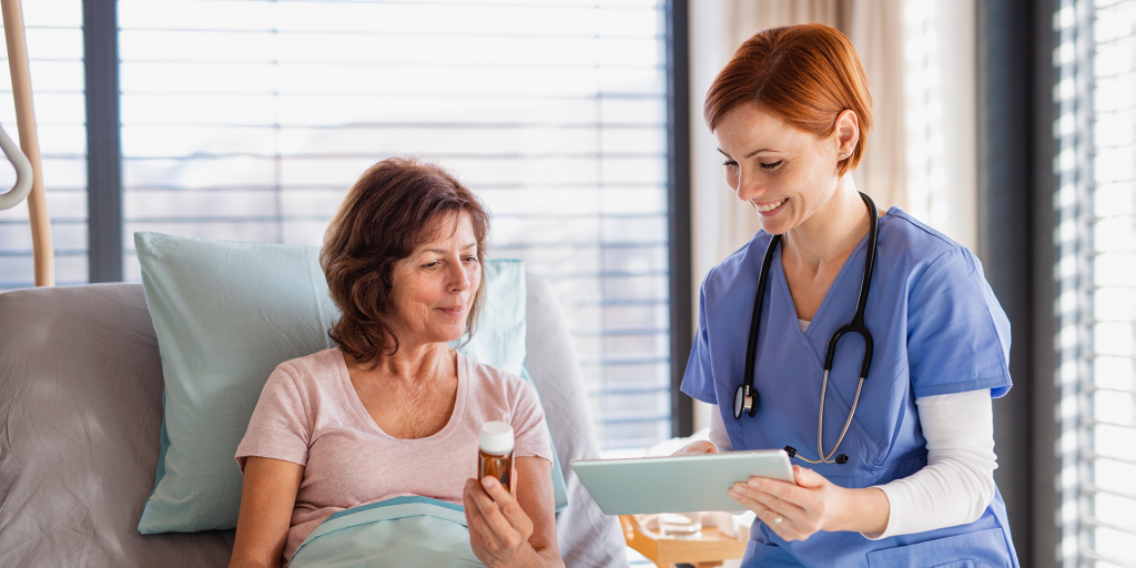 A female doctor with tablet talking to patient in bed in hospital MOBILE discharge summaries